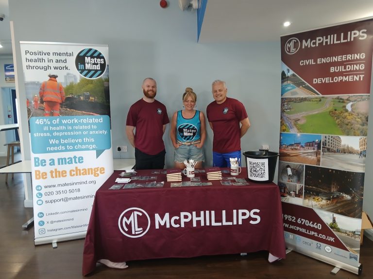 Three people stood behind a table and signs promoting a charity event.