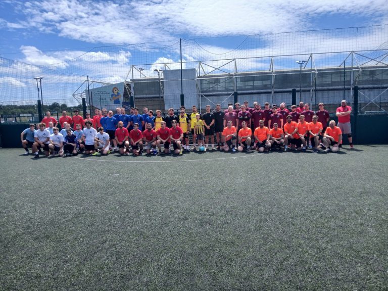 A group of people pose for a photo at a charity football match.