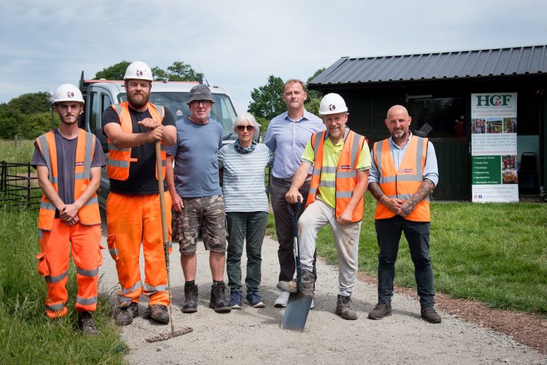 Six people stood for a photograph. Some wearing high-vis and hardhats holding shovels and rakes.