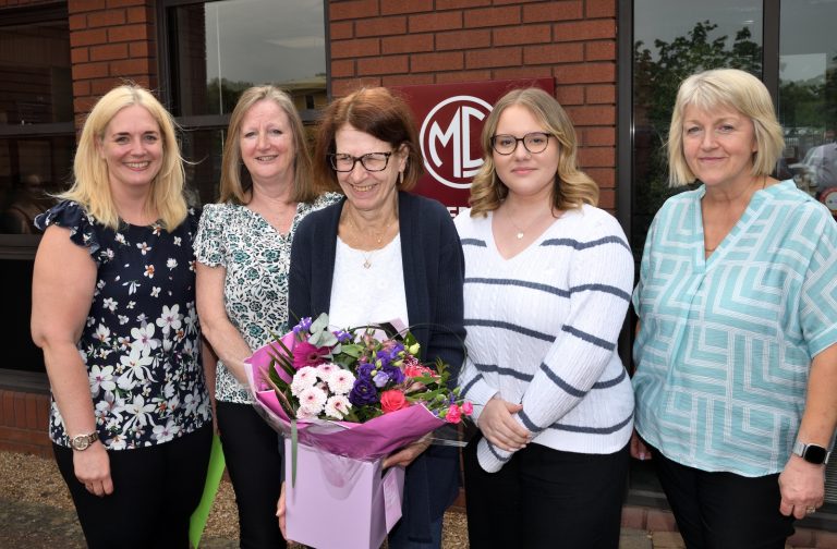 Five people stood together for a photograph. The middle person is holding a bouquet of flowers.