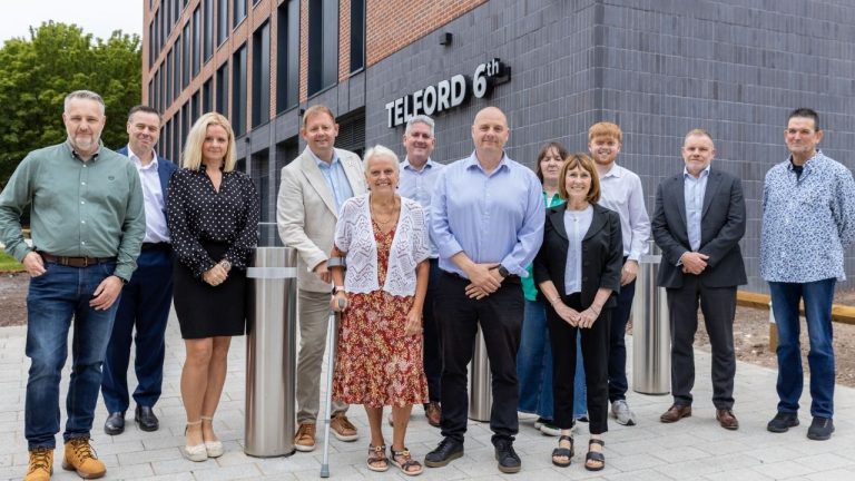 12 people stood together in a line outside of a newly build academic building.
