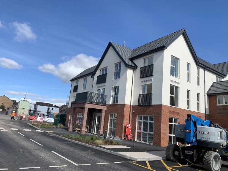 The exterior of an apartment building. The building is brand new and there is still construction vehicles and equipment outside of it. 